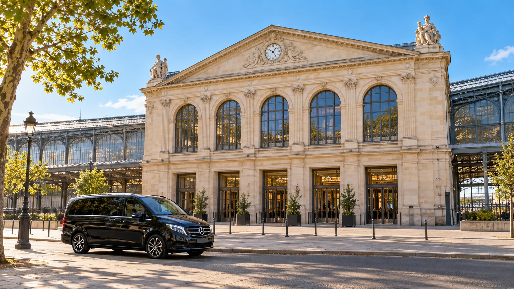 A black van outside a station facade with five arched windows and a long sunlit glass train shed